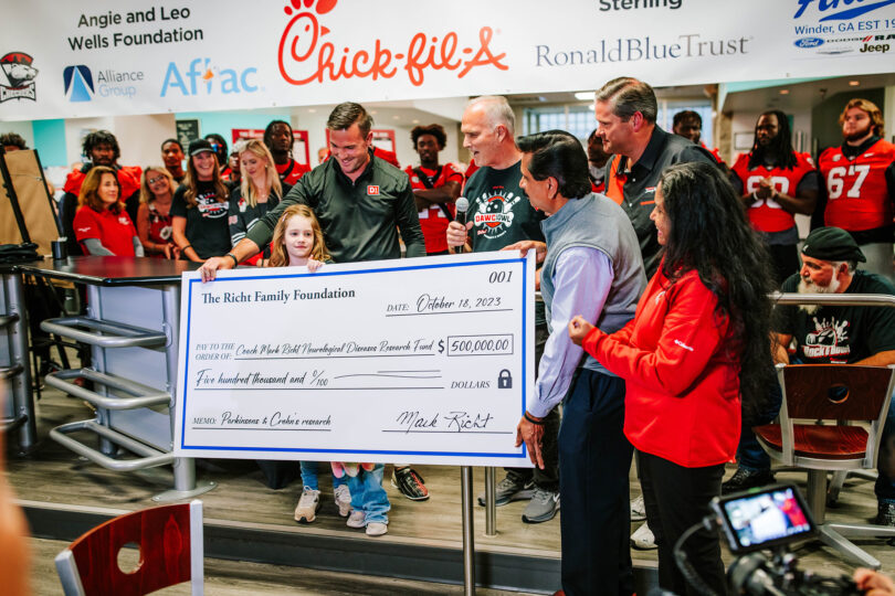 Coach Mark Richt speaks as he and his family present Anumantha Kanthasamy (holding check, at right) with a gift of $500,000 from The Richt Family Foundation, the donation which launched the 2023 Chick-fil-A Dawg Bowl fundraising campaign. (Photo by Repurposed Photography.)