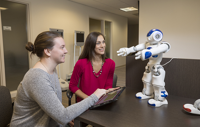l-r: Graduate student Kasey Smith and professor Jenay Beer looking at interactive companion robots in the Beers lab.