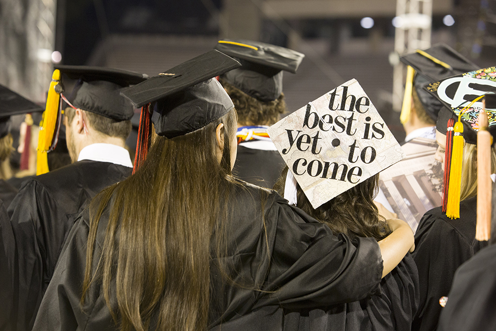 Detail of a decorated motherboard and a student putting her arm around another student during the 2016 Spring Undergraduate Commencement Ceremony.